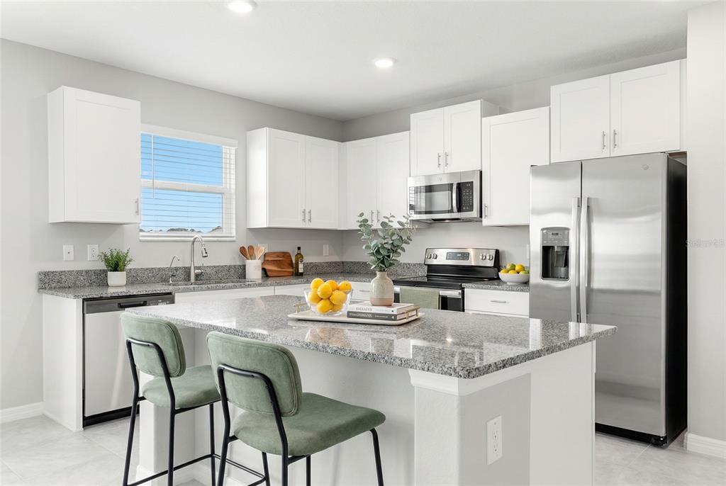 A modern kitchen features white cabinets, granite countertops, stainless steel appliances, and a breakfast island — 5351 NIGHT TIDE LANE, WIMAUMA, FL