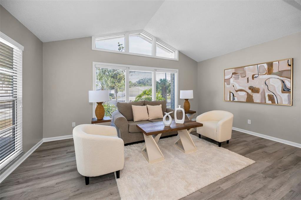 A living room features gray wood-look flooring, a beige sofa, two white chairs, and artwork — 7404 CLEARVIEW DRIVE, TAMPA, FL