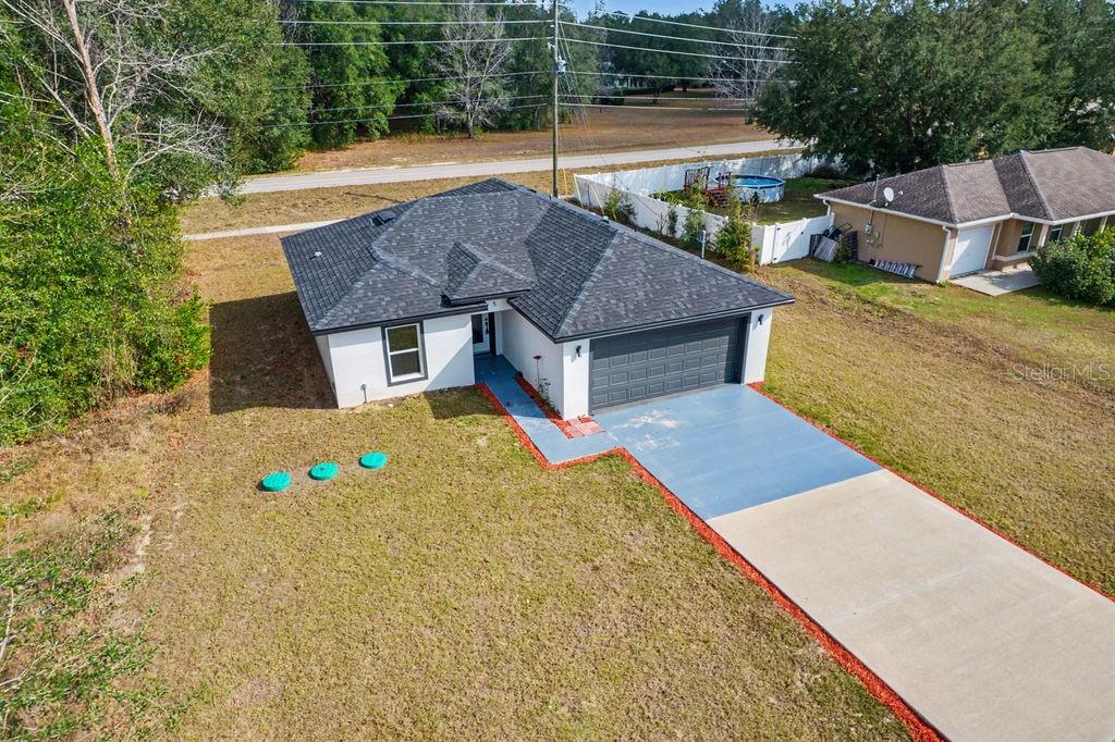 An aerial view of a single-story house with a dark roof and a concrete driveway — 5 PINE TRACK PLACE, OCALA, FL