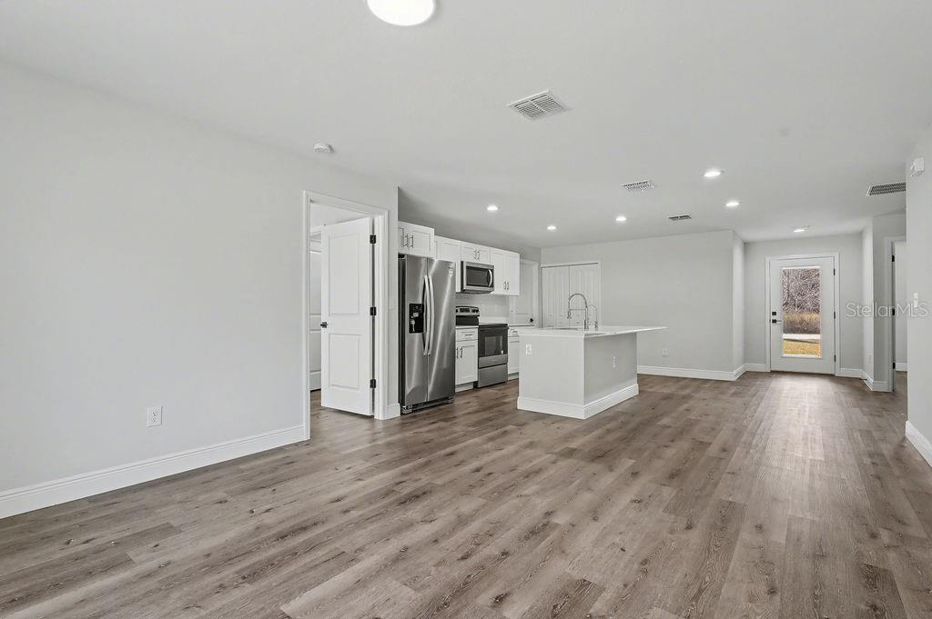 An open-concept kitchen and living area features white cabinetry, stainless steel appliances, and wood-look flooring — 5 PINE TRACK PLACE, OCALA, FL