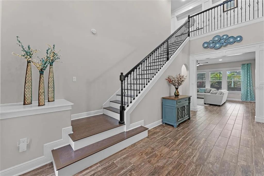 A staircase with dark wood treads and a black railing stands in a tiled foyer — 14312 SUNBRIDGE CIRCLE, WINTER GARDEN, FL