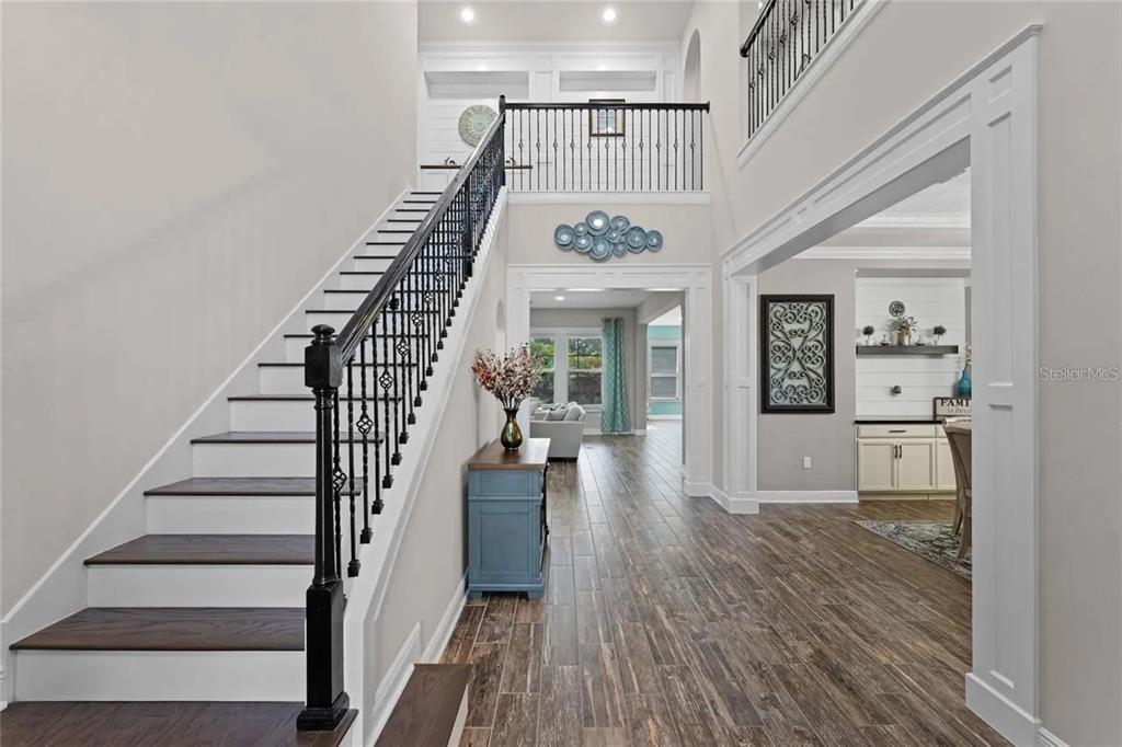 A foyer features a staircase with black railings, wood-look tile floors, and an open layout — 14312 SUNBRIDGE CIRCLE, WINTER GARDEN, FL