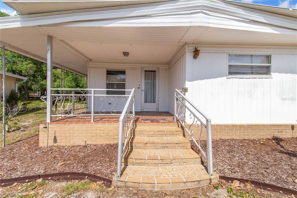 A mobile home exterior features a covered porch with metal railings and brick steps — 31 WOODLAND CIRCLE, HAINES CITY, FL