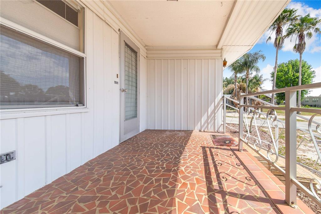 A covered porch features a red tile floor and a white metal railing — 31 WOODLAND CIRCLE, HAINES CITY, FL