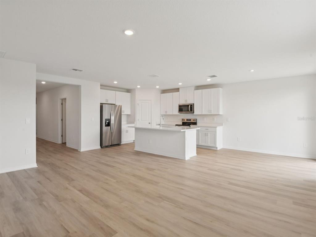 An open-concept kitchen features white cabinetry, stainless steel appliances, and light wood-look flooring — 1789 FOREST RUN LANE, AUBURNDALE, FL
