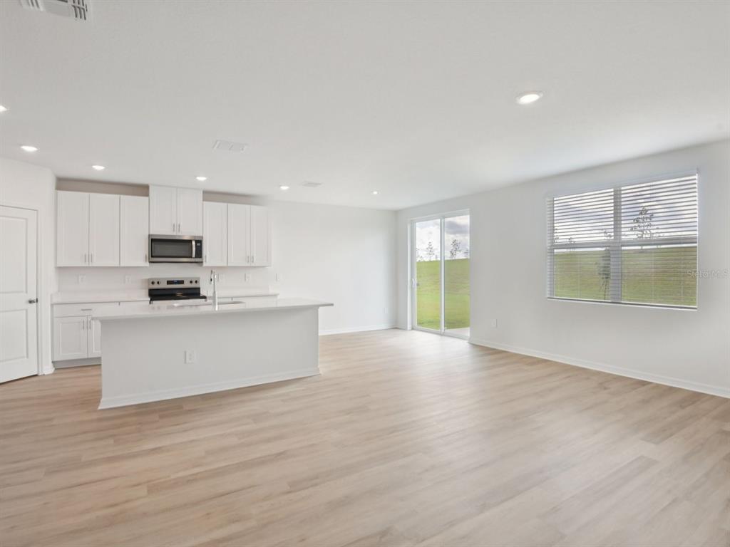 An open-concept kitchen and living area with white cabinets, a central island, and light flooring — 1789 FOREST RUN LANE, AUBURNDALE, FL