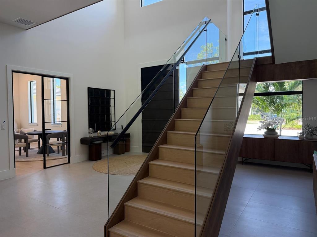 A modern foyer features a light wood staircase with a glass railing and a black-framed doorway — 15544 PENDIO DRIVE, BELLA COLLINA, FL