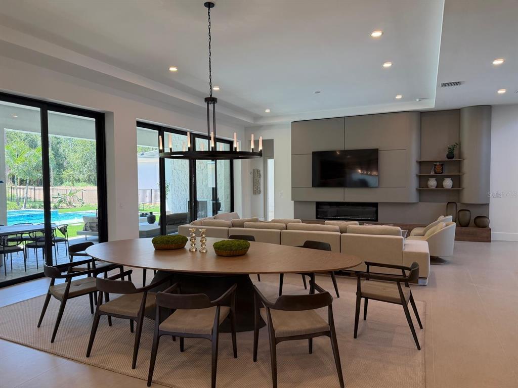 A modern open-concept living and dining area features a large oval table and a sectional sofa — 15544 PENDIO DRIVE, BELLA COLLINA, FL