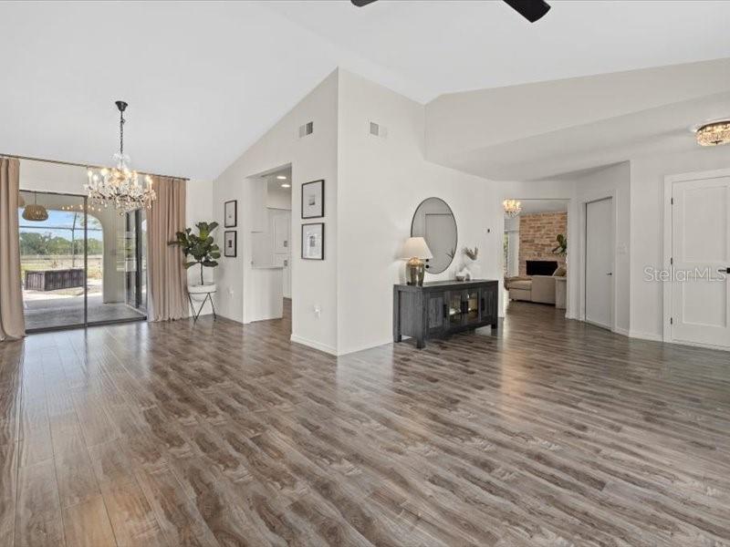 A spacious living area features wood-look flooring, vaulted ceilings, a chandelier, and a sliding glass door — 15650 PRAIRIE CREEK BOULEVARD, PUNTA GORDA, FL