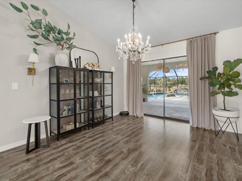 A dining room features a crystal chandelier, glass-front cabinets, wood-look tile floors, and a pool view — 15650 PRAIRIE CREEK BOULEVARD, PUNTA GORDA, FL