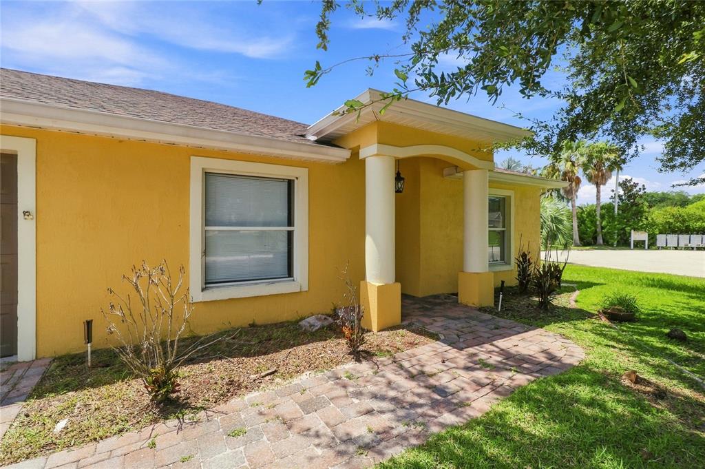 A yellow house exterior features a brick walkway leading to a covered porch with columns — 106 MAJESTIC GARDENS COURT, WINTER HAVEN, FL