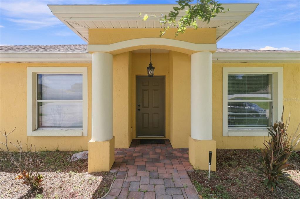A yellow house exterior features a covered entryway with two white columns and a brick walkway — 106 MAJESTIC GARDENS COURT, WINTER HAVEN, FL