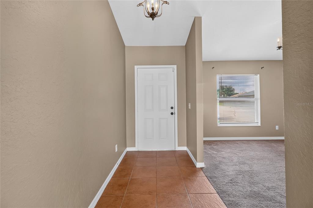 An entryway with brown tile flooring leads to a white front door and carpeted room — 106 MAJESTIC GARDENS COURT, WINTER HAVEN, FL