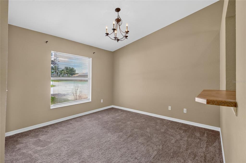 An empty room with beige walls, brown carpeting, a window with blinds, and a chandelier — 106 MAJESTIC GARDENS COURT, WINTER HAVEN, FL