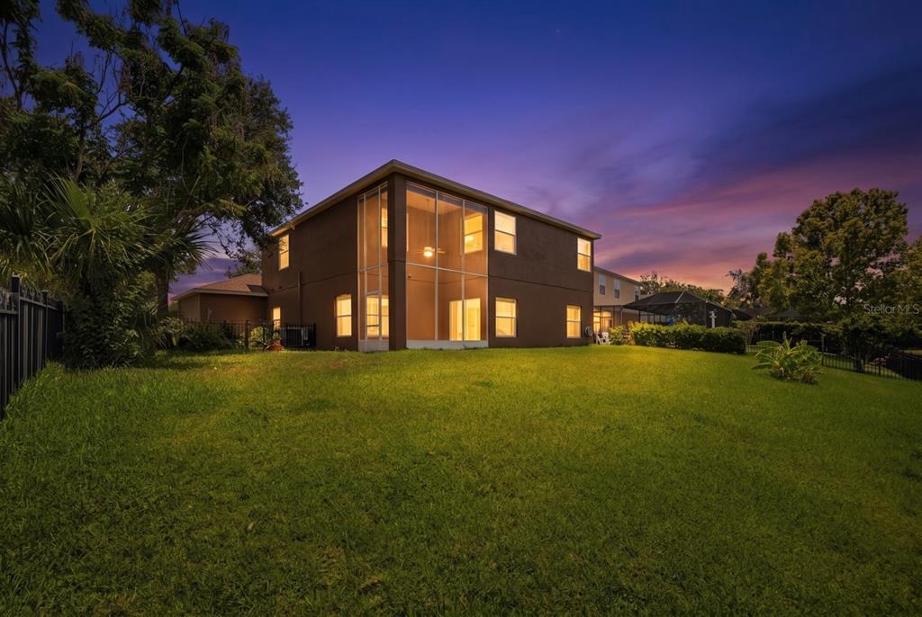 The rear exterior of a two-story house features a large screened-in lanai at twilight — 14722 HERONGLEN DRIVE, LITHIA, FL