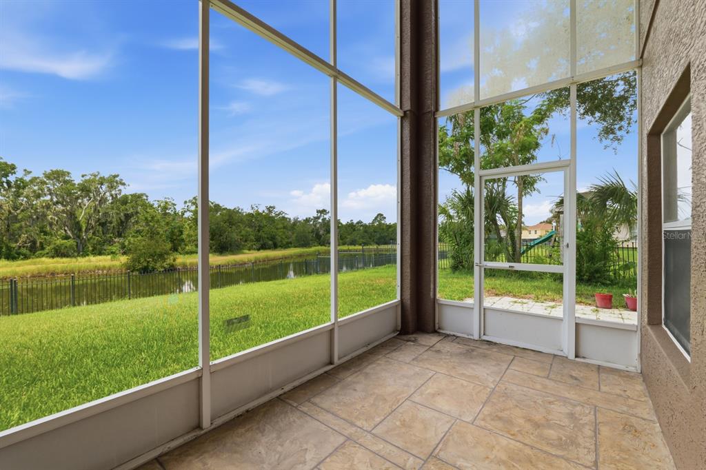 A screened-in patio with tile flooring overlooks a grassy backyard and a small pond — 14722 HERONGLEN DRIVE, LITHIA, FL