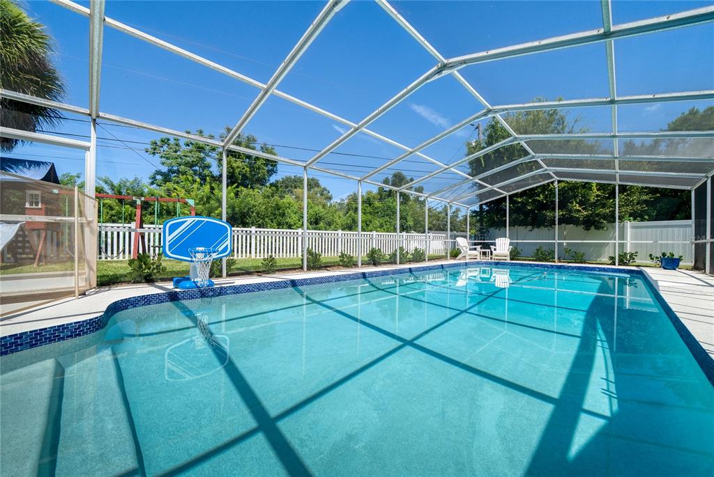 A screened-in swimming pool with a basketball hoop sits in a backyard with a fence — 433 GILBERT ROAD, WINTER PARK, FL