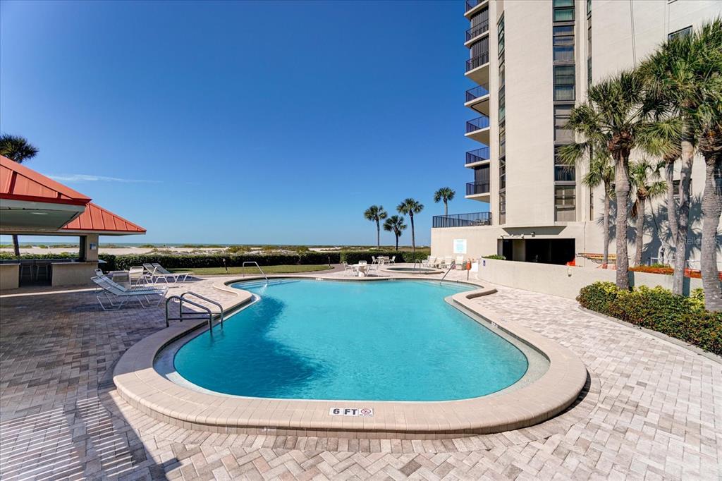 A swimming pool sits on a paved patio next to a high-rise building and beach — 1290 GULF BOULEVARD UNIT 1406, CLEARWATER, FL