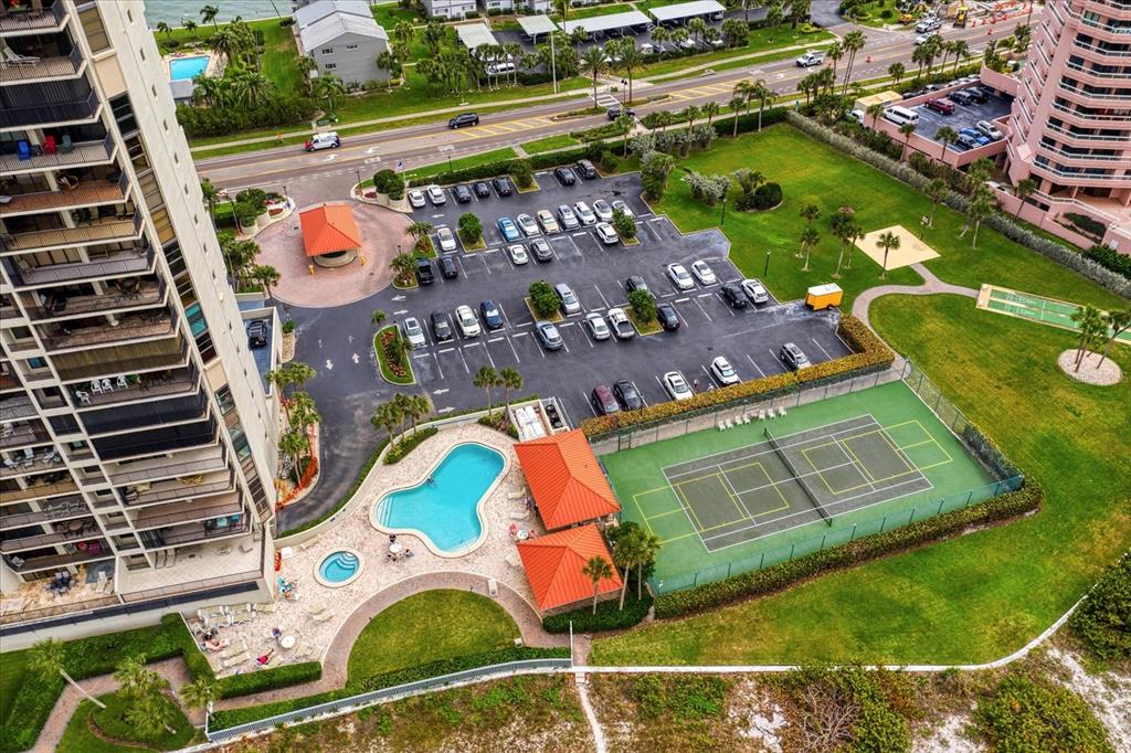 An aerial view shows a high-rise building, a parking lot, a swimming pool, and tennis courts — 1290 GULF BOULEVARD UNIT 1406, CLEARWATER, FL