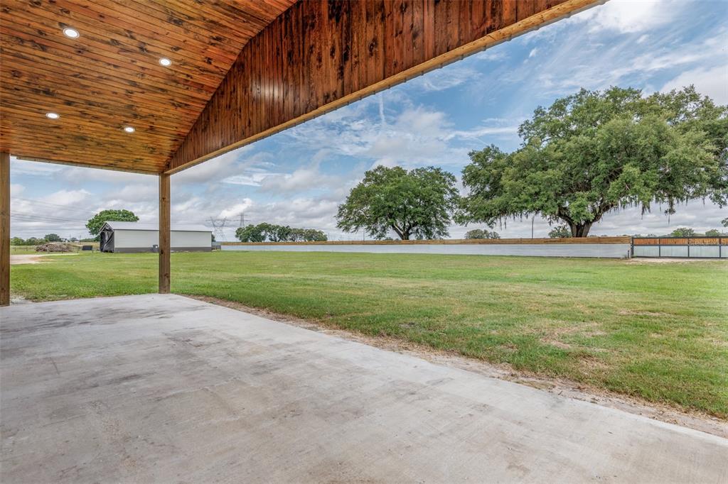 A covered concrete patio overlooks a large grassy yard with mature trees and a fence — 1285 102ND BLVD A UNIT (Option 1), WILDWOOD, FL