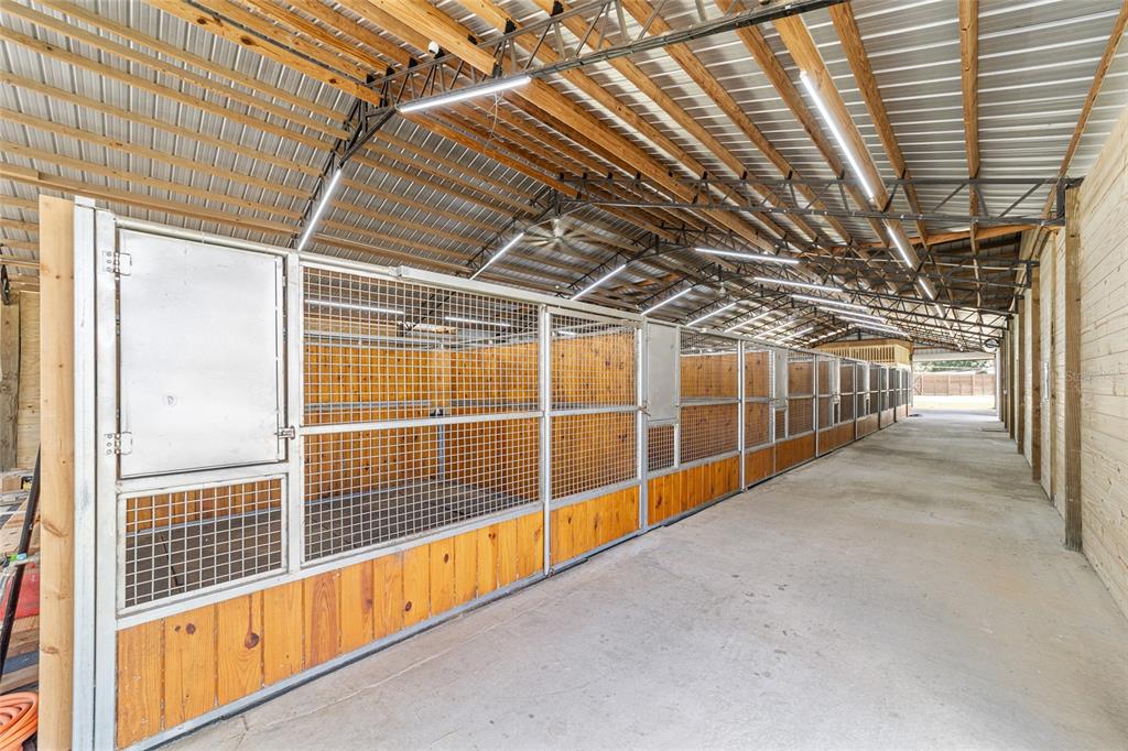 A long indoor horse stable aisle features multiple stalls with wood paneling and metal mesh — 1285 102ND BLVD A UNIT (Option 1), WILDWOOD, FL