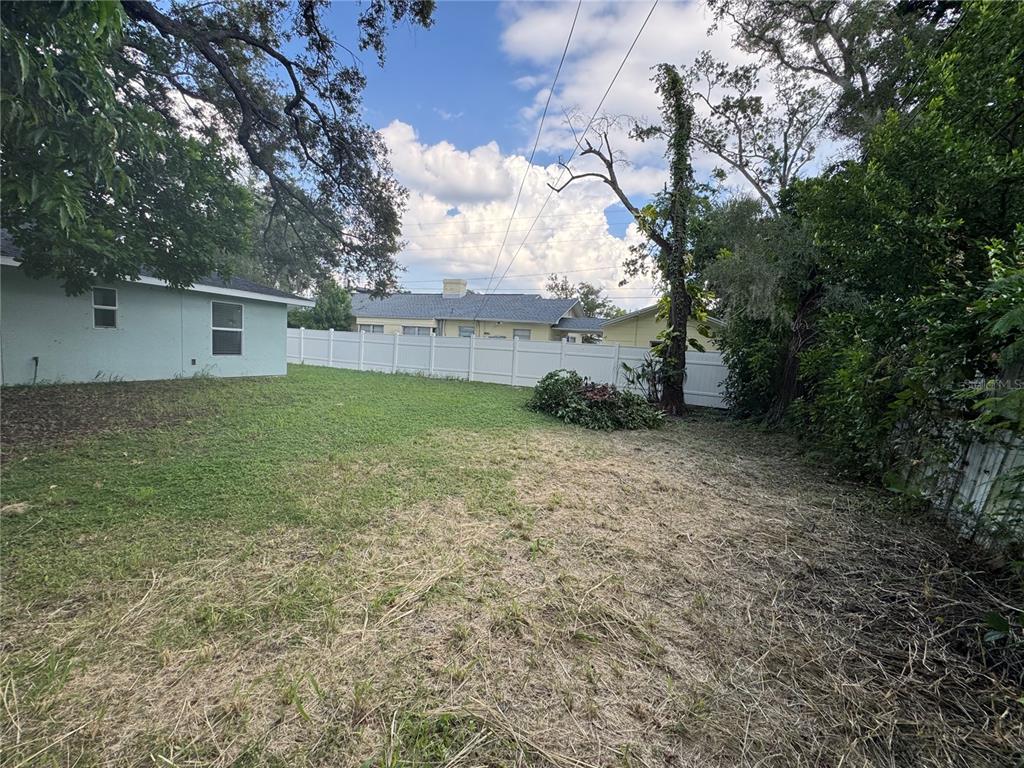 A backyard with a white vinyl fence, a small concrete pad, and a light blue house — 1493 CLEVELAND STREET, CLEARWATER, FL
