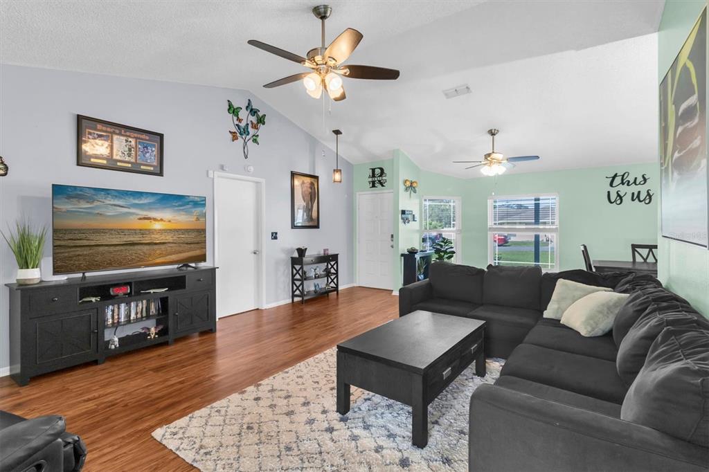 A living room features a dark sectional sofa, a television on a console, and ceiling fans — 10513 BLYTHVILLE ROAD, SPRING HILL, FL