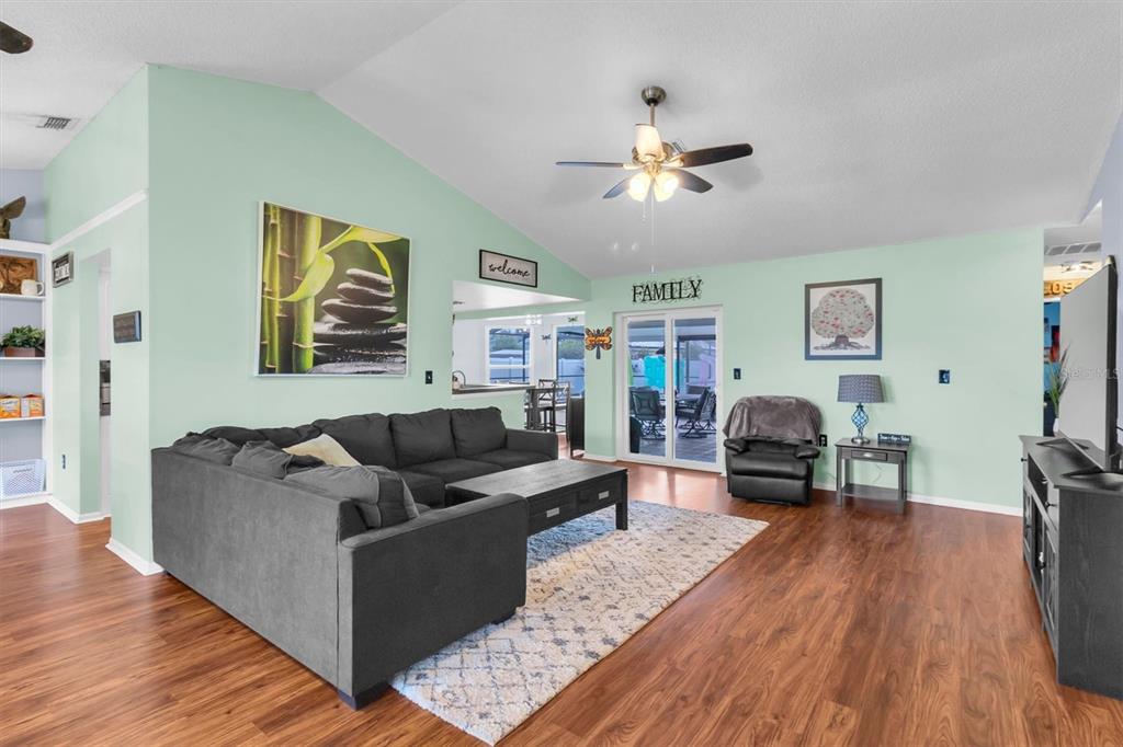 A living room features light green walls, a dark sectional sofa, and wood-look flooring — 10513 BLYTHVILLE ROAD, SPRING HILL, FL