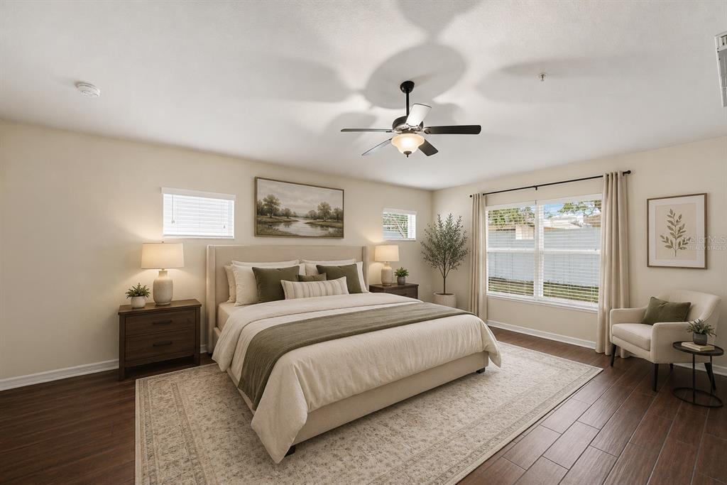 A bedroom features a king-sized bed, dark wood flooring, a ceiling fan, and large windows — 13368 MANDALAY PLACE, SPRING HILL, FL