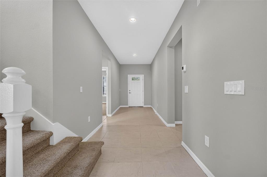 A hallway with tile flooring, gray walls, and a carpeted staircase on the left — 8924 BENGAL COURT, KISSIMMEE, FL