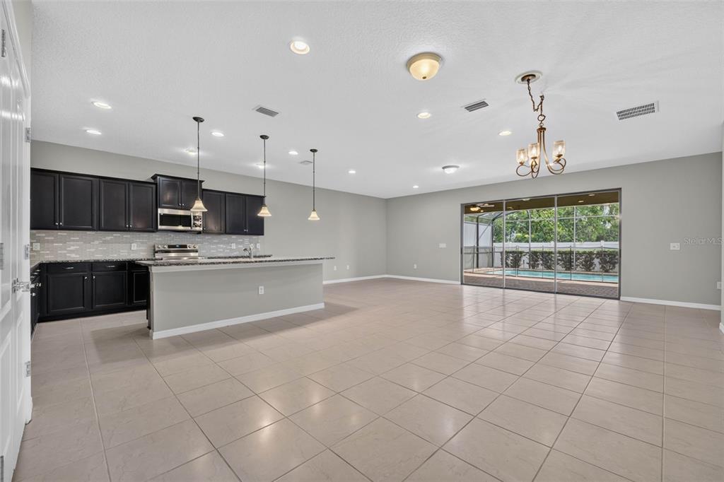 A kitchen with dark cabinets and an island opens into a large tiled living area — 8924 BENGAL COURT, KISSIMMEE, FL
