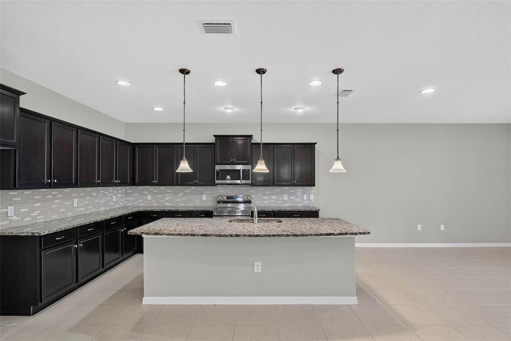A kitchen features dark wood cabinets, granite countertops, a central island, and three pendant lights — 8924 BENGAL COURT, KISSIMMEE, FL