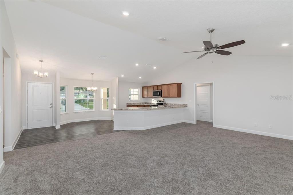 An open-concept living area features gray carpeting, a kitchen with wood cabinets, and dining space — 23 RAMROCK LANE, PALM COAST, FL