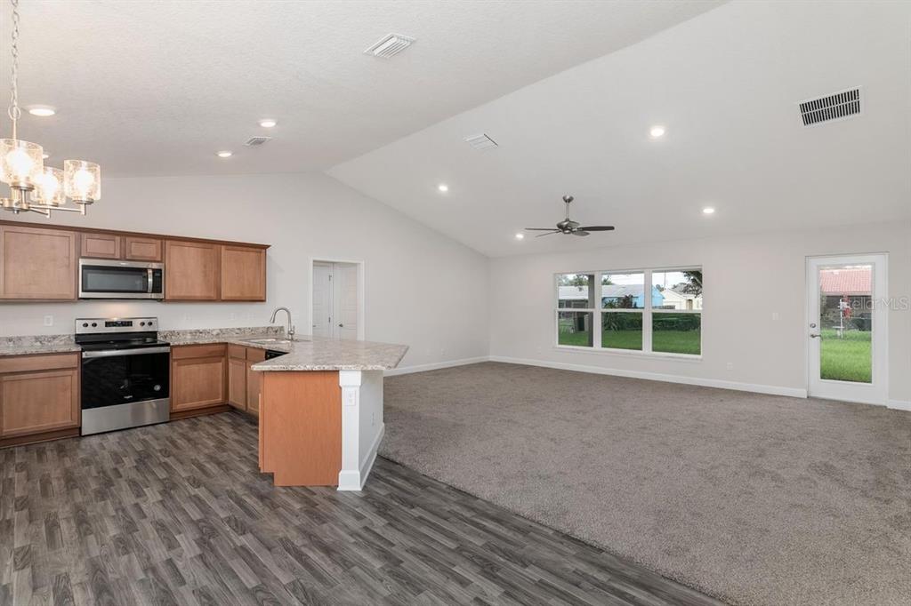 An open-concept kitchen with wood cabinets and a living area with carpet and vaulted ceilings — 23 RAMROCK LANE, PALM COAST, FL