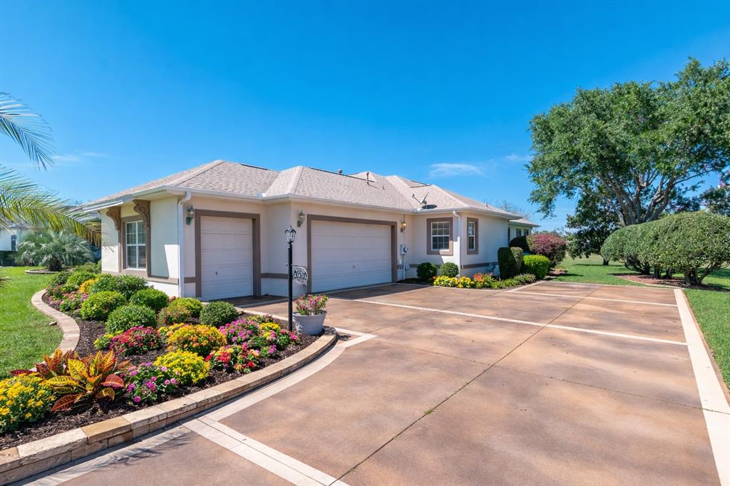 A beige house with a two-car garage and a landscaped front yard under a blue sky — 1670 SAINT JAMES CIRCLE, THE VILLAGES, FL