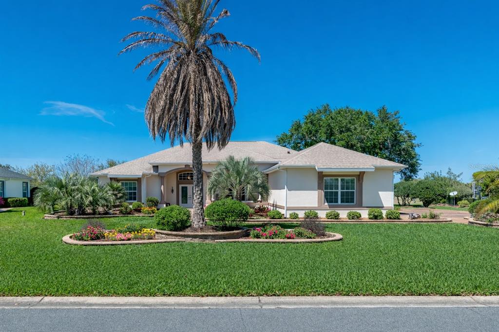A single-story house with a palm tree, landscaped garden, and lawn under a blue sky — 1670 SAINT JAMES CIRCLE, THE VILLAGES, FL