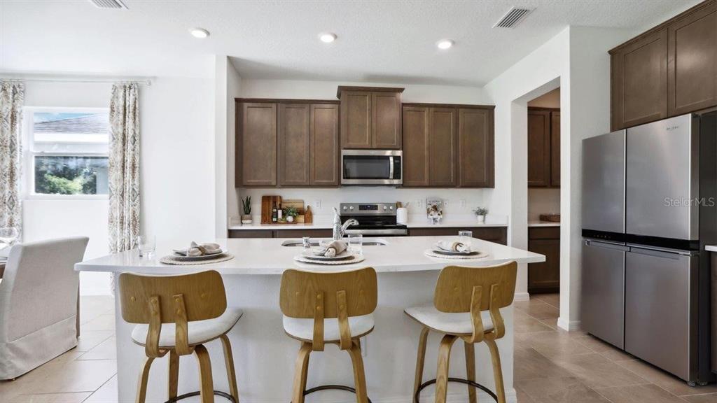 A kitchen features dark wood cabinets, stainless steel appliances, and a white quartz island — 35611 LOWERY TRAIL, ZEPHYRHILLS, FL