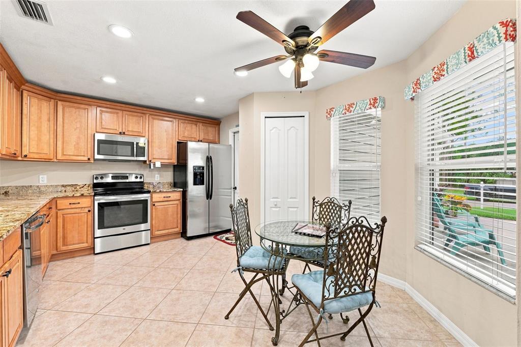 A kitchen features light wood cabinets, stainless steel appliances, tile flooring, and a small dining area — 1531 DALLAM AVENUE NW, PALM BAY, FL