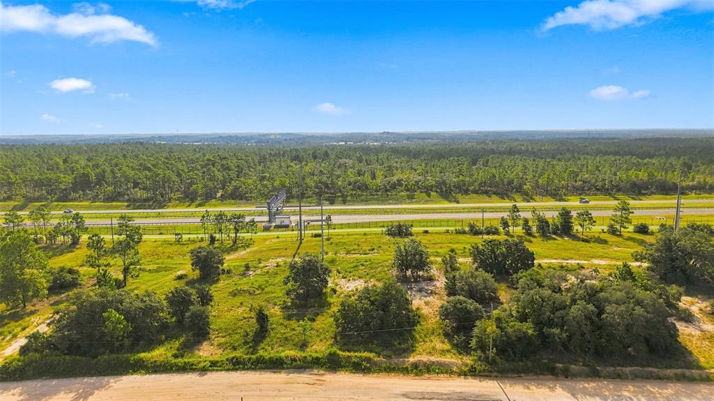 An aerial view shows a vacant, grassy lot bordering a highway with a dense forest beyond — 5050 W HOSKINS LANE, LECANTO, FL