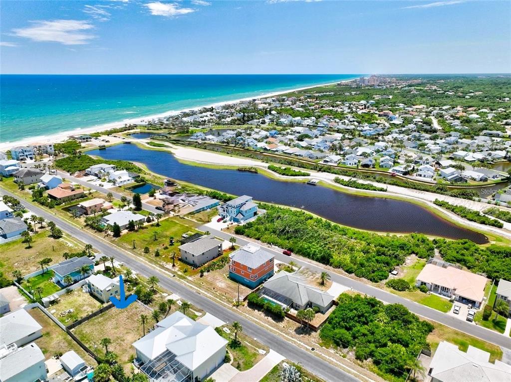 An aerial view shows a coastal neighborhood with houses, a long pond, and the ocean — 47 ROLLINS DRIVE, PALM COAST, FL