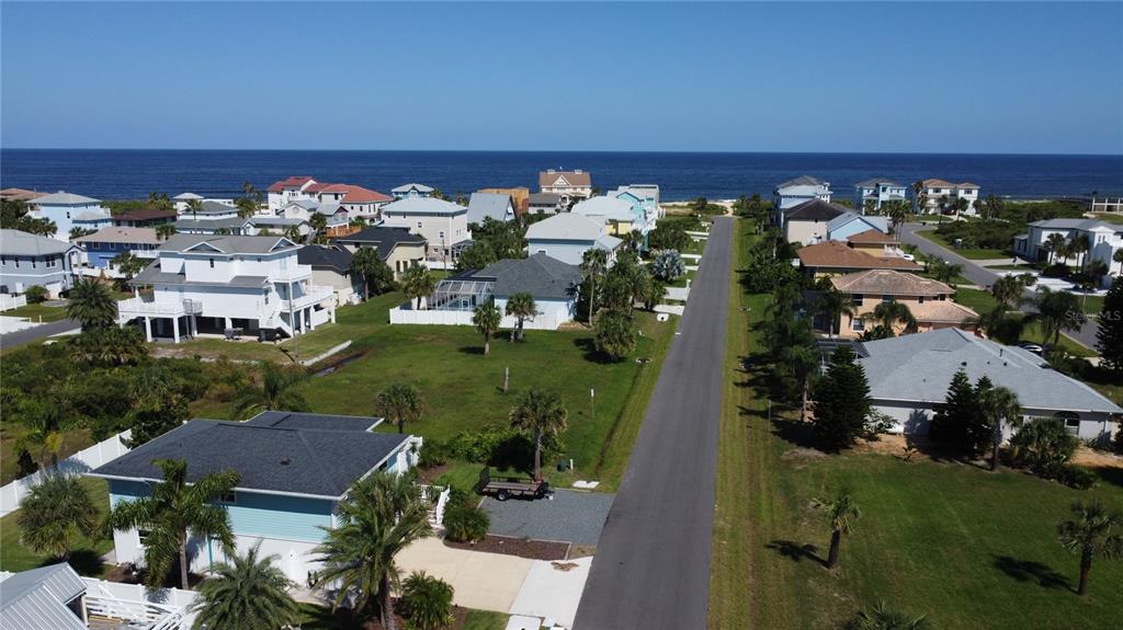 An aerial view shows a coastal neighborhood with houses, a paved road, and the ocean — 47 ROLLINS DRIVE, PALM COAST, FL