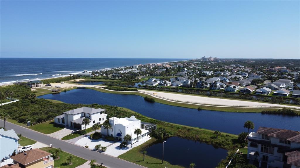 An aerial view shows a coastal neighborhood with houses, a winding pond, and the ocean — 47 ROLLINS DRIVE, PALM COAST, FL