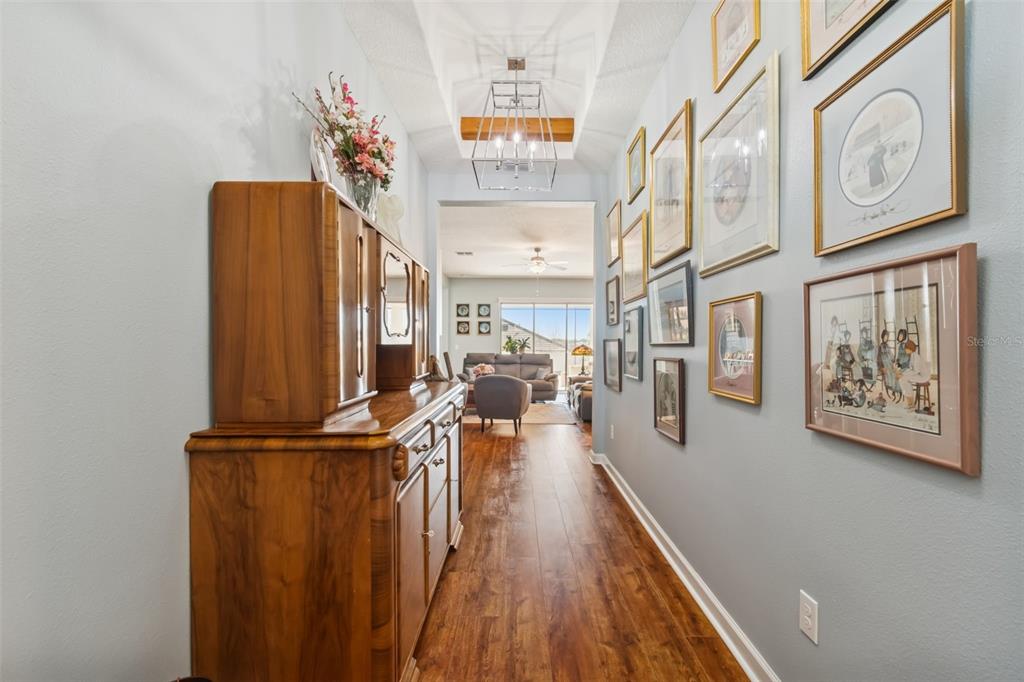 A hallway with wood flooring, a wooden hutch, and a gallery wall leads to a living room — 31516 CABANA RYE, SAN ANTONIO, FL