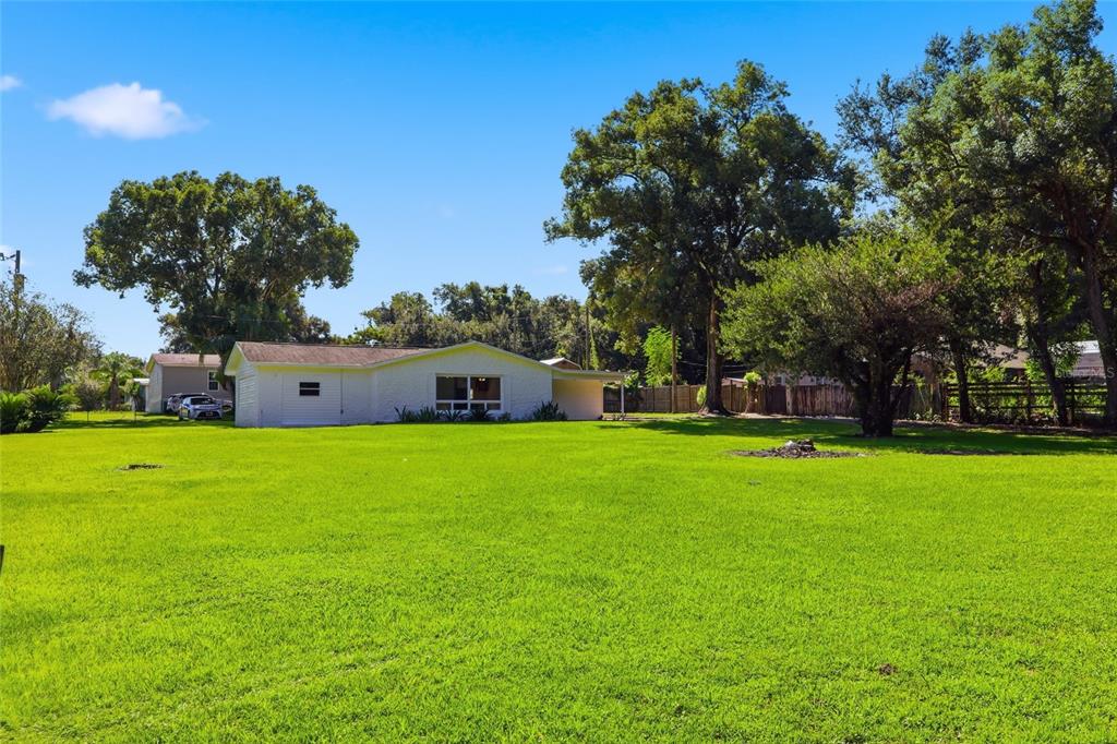 A white, single-story house sits on a large, grassy lot surrounded by mature trees — 39250 MIRAMAR DRIVE, ZEPHYRHILLS, FL