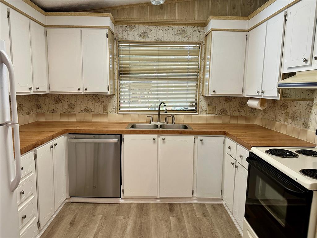 A kitchen with white cabinets, wood-look countertops, a stainless steel dishwasher, and floral wallpaper — 322 BASS COURT, OLDSMAR, FL