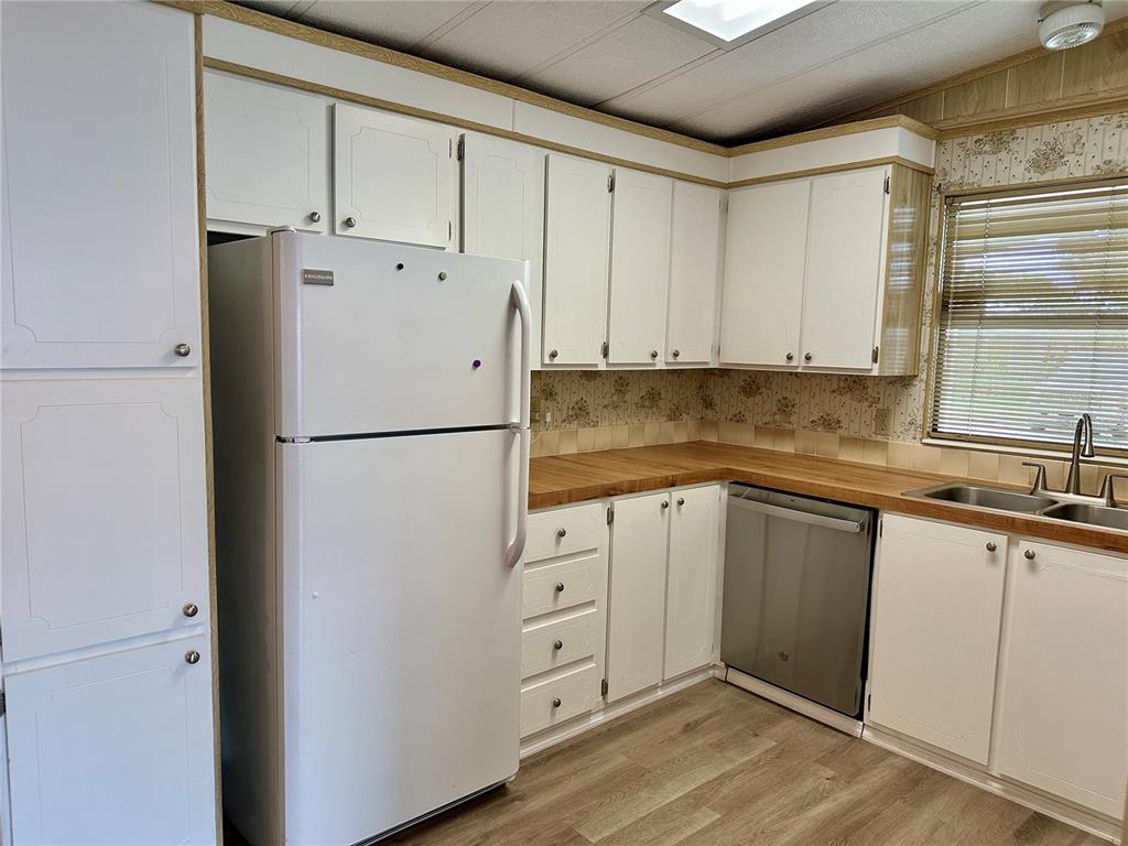 A kitchen features white cabinets, wood-look countertops, a stainless steel dishwasher, and a white refrigerator — 322 BASS COURT, OLDSMAR, FL