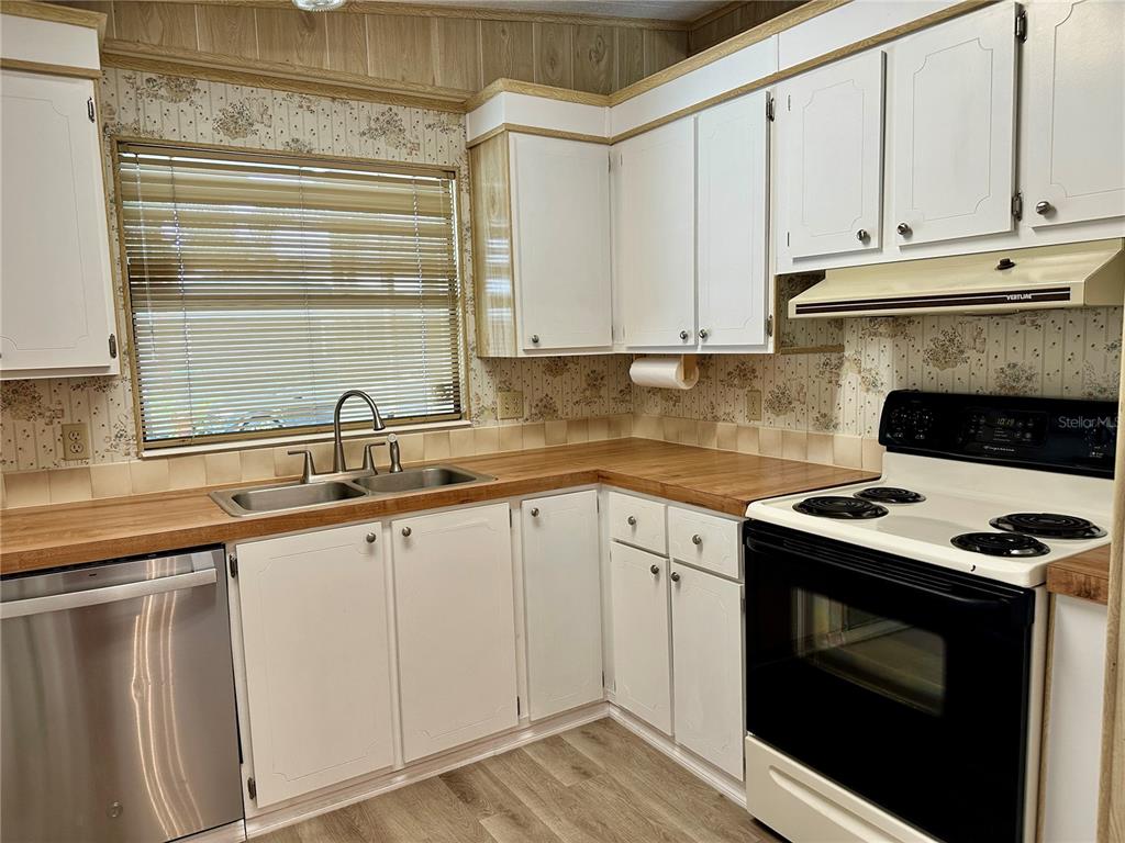 A kitchen features white cabinets, wood countertops, a stainless steel dishwasher, and floral wallpaper — 322 BASS COURT, OLDSMAR, FL