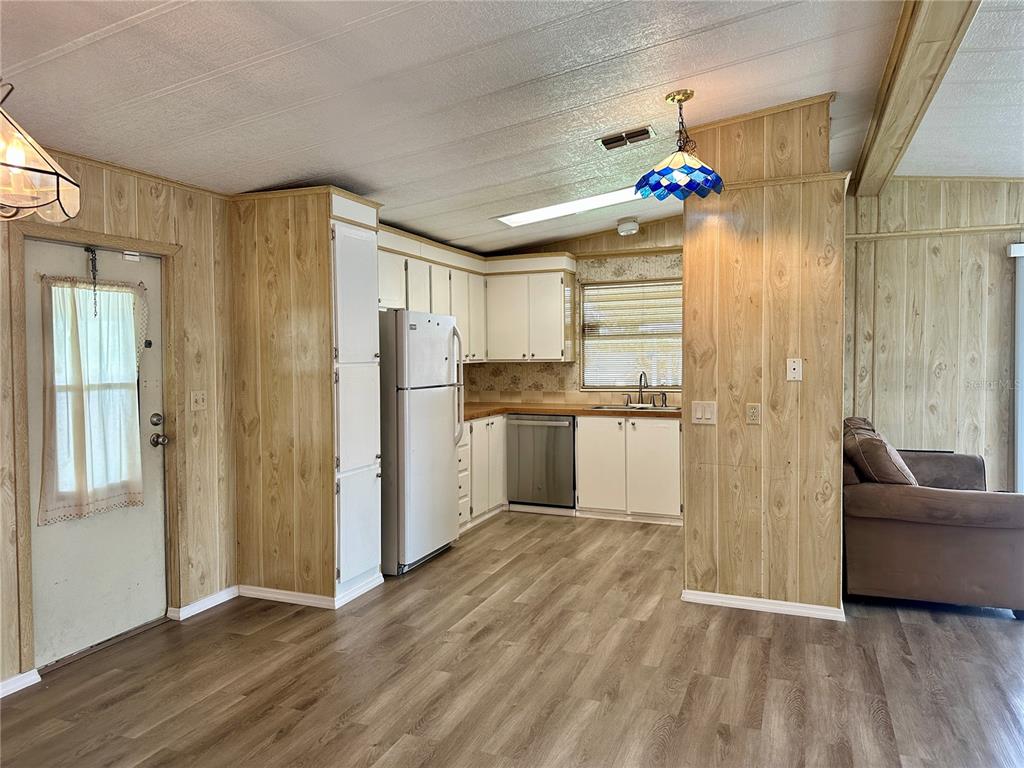 A kitchen with wood-paneled walls, white cabinets, stainless steel appliances, and wood-look flooring — 322 BASS COURT, OLDSMAR, FL