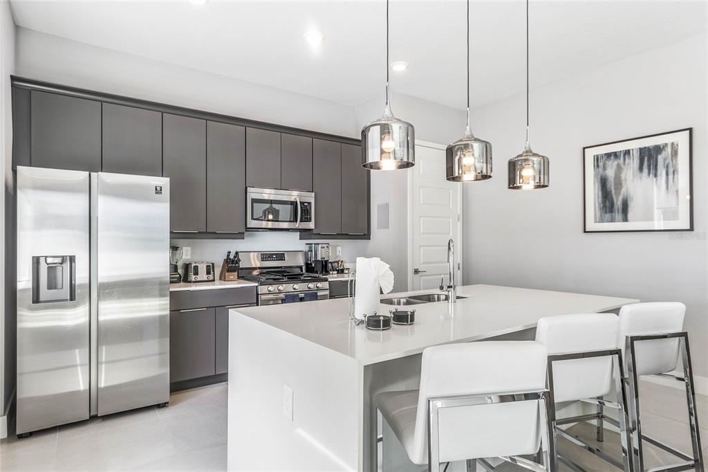 A modern kitchen features dark gray cabinetry, stainless steel appliances, and a white quartz island — 7770 SANDY RIDGE DRIVE UNIT 110, REUNION, FL