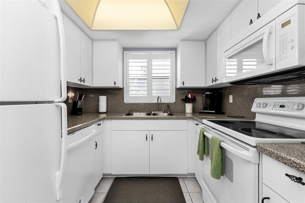 A white kitchen features granite countertops, white cabinetry, and a window above the sink — 1730 MANASOTA BEACH ROAD UNIT 115, ENGLEWOOD, FL